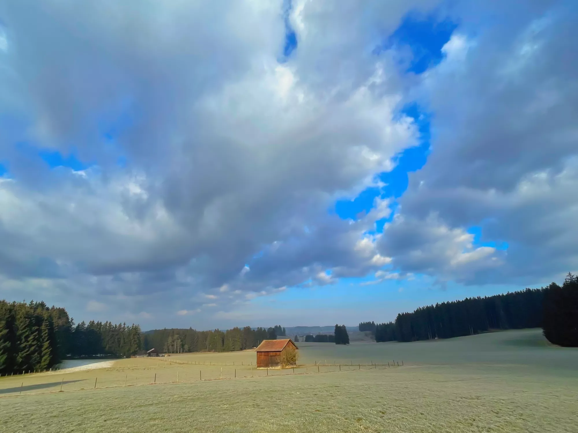 Sanfte Hügel und offene Felder rund um Aitrang im wechselnden Licht des Tages.