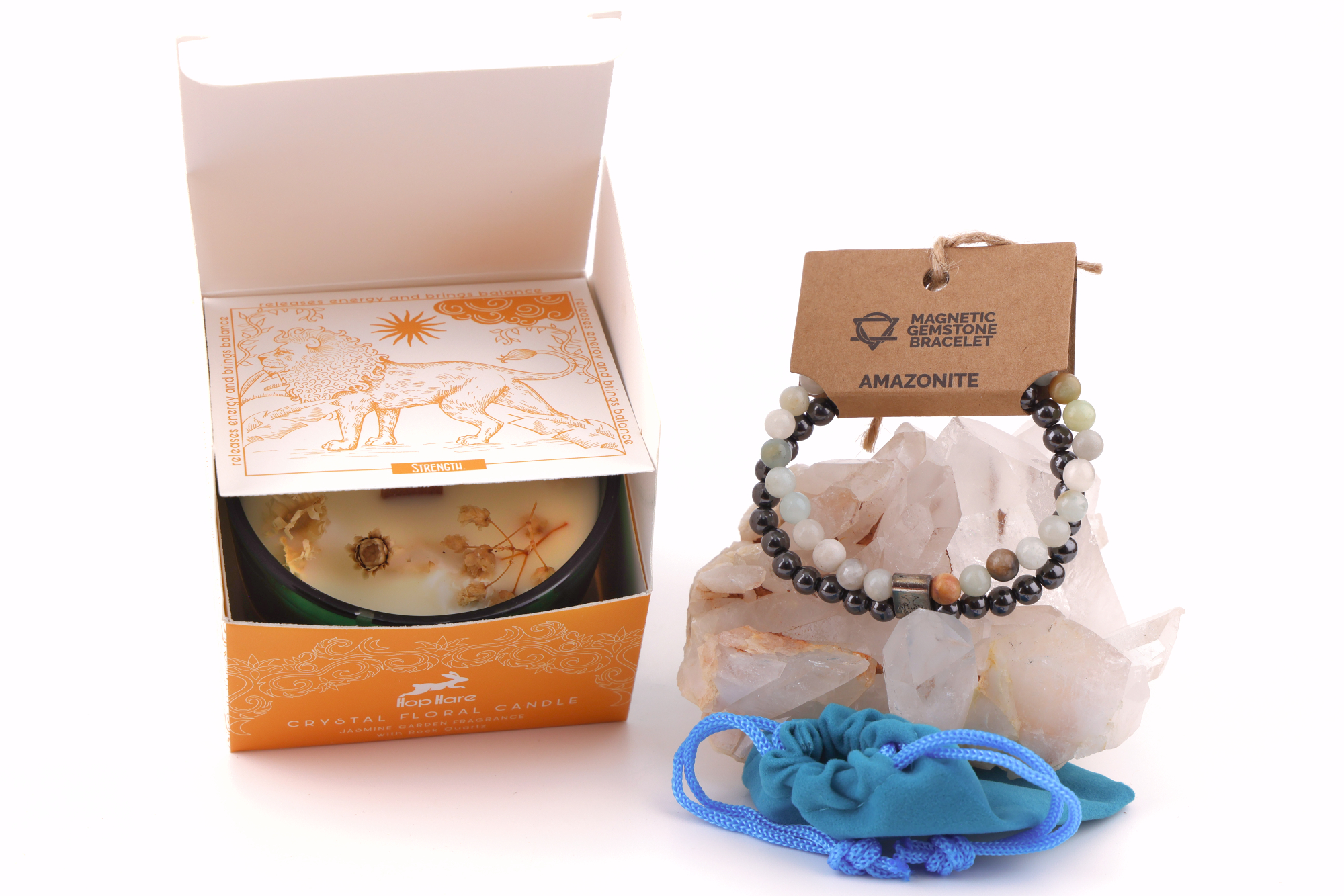 Amazonit‑Magnetarmband auf einem klaren Bergkristall‑Cluster, daneben eine Duftkerze mit floralen Elementen in einer orangefarbenen Verpackung sowie ein blaues Stoffbeutelchen.