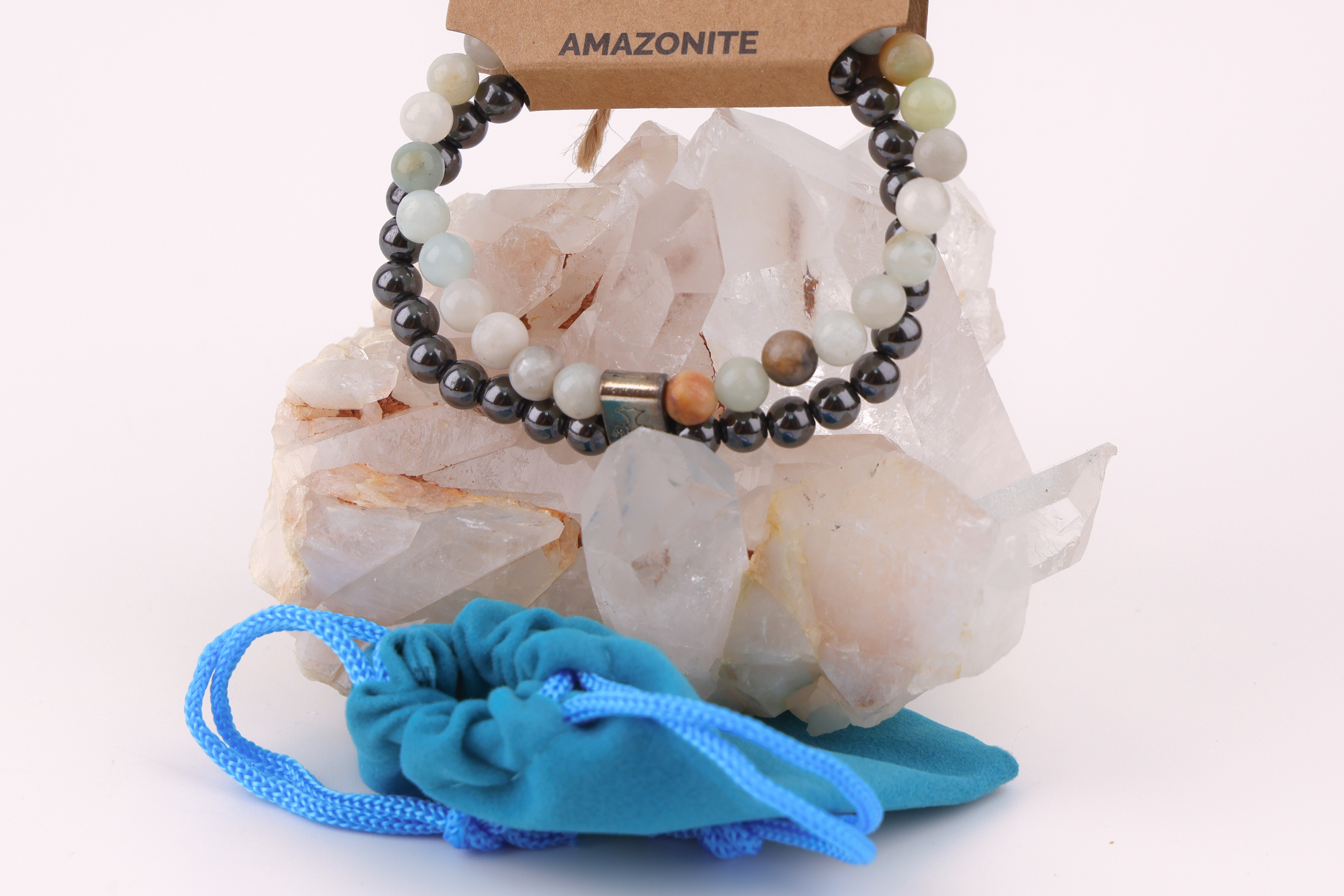 Sodalith‑Magnetarmband mit schwarzen und hellen Edelsteinperlen, dekorativ präsentiert auf einem klaren Bergkristall‑Cluster; davor ein türkisfarbenes Stoffbeutelchen mit blauen Zugbändern.