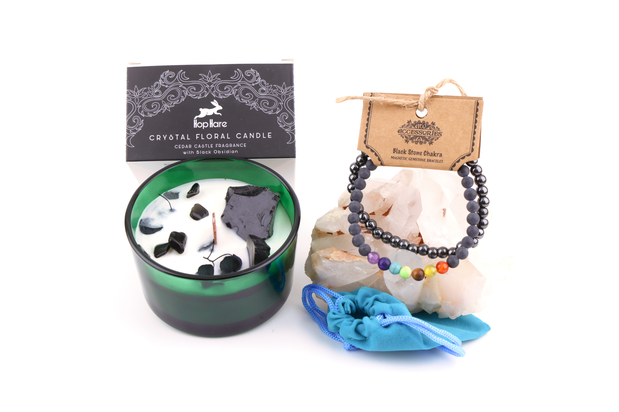Ein grünes Glas mit einer weißen Hop Hare „Der König der Schwerter“-Blumenkerze, dekoriert mit schwarzem Obsidian, Blättern und Holzdocht, daneben ein Schwarzstein‑Chakra‑Magnetarmband auf klaren Bergkristallen sowie ein türkisfarbener Stoffbeutel – alles auf weißem Hintergrund arrangiert.