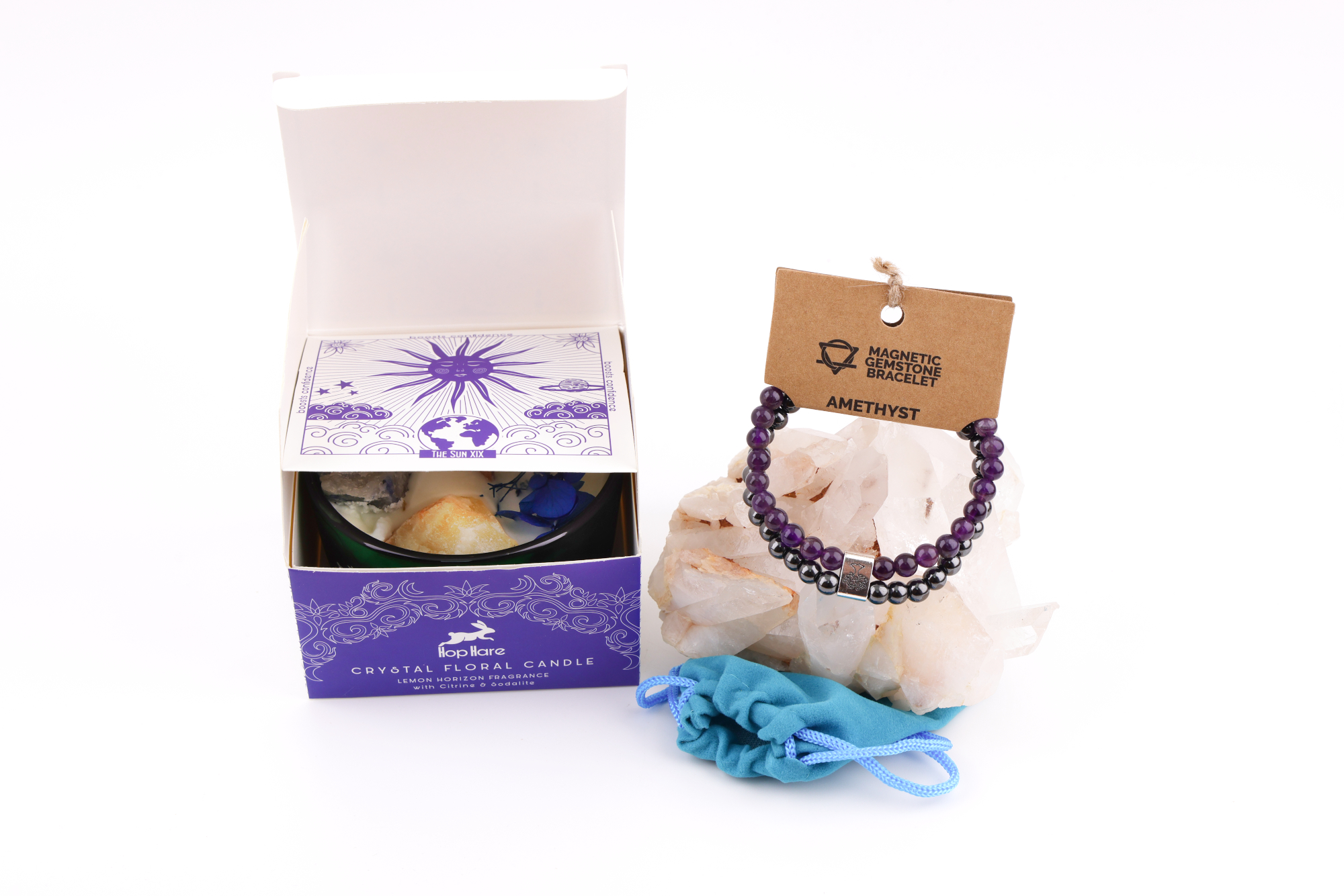 Grüne Hop‑Hare Duftkerze mit Citrin‑ und Amethyst‑Steinen sowie Blüten, daneben die lilafarbene Produktbox; rechts ein Amethyst‑Magnetarmband auf brauner Karte, präsentiert auf Bergkristallen mit türkisfarbenem Beutel.