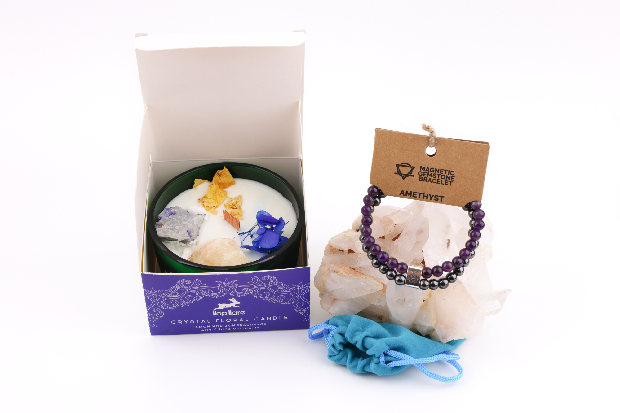 Grüne Hop‑Hare Duftkerze mit Citrin‑ und Amethyst‑Steinen sowie Blüten, daneben die lilafarbene Produktbox; rechts ein Amethyst‑Magnetarmband auf brauner Karte, präsentiert auf Bergkristallen mit türkisfarbenem Beutel.