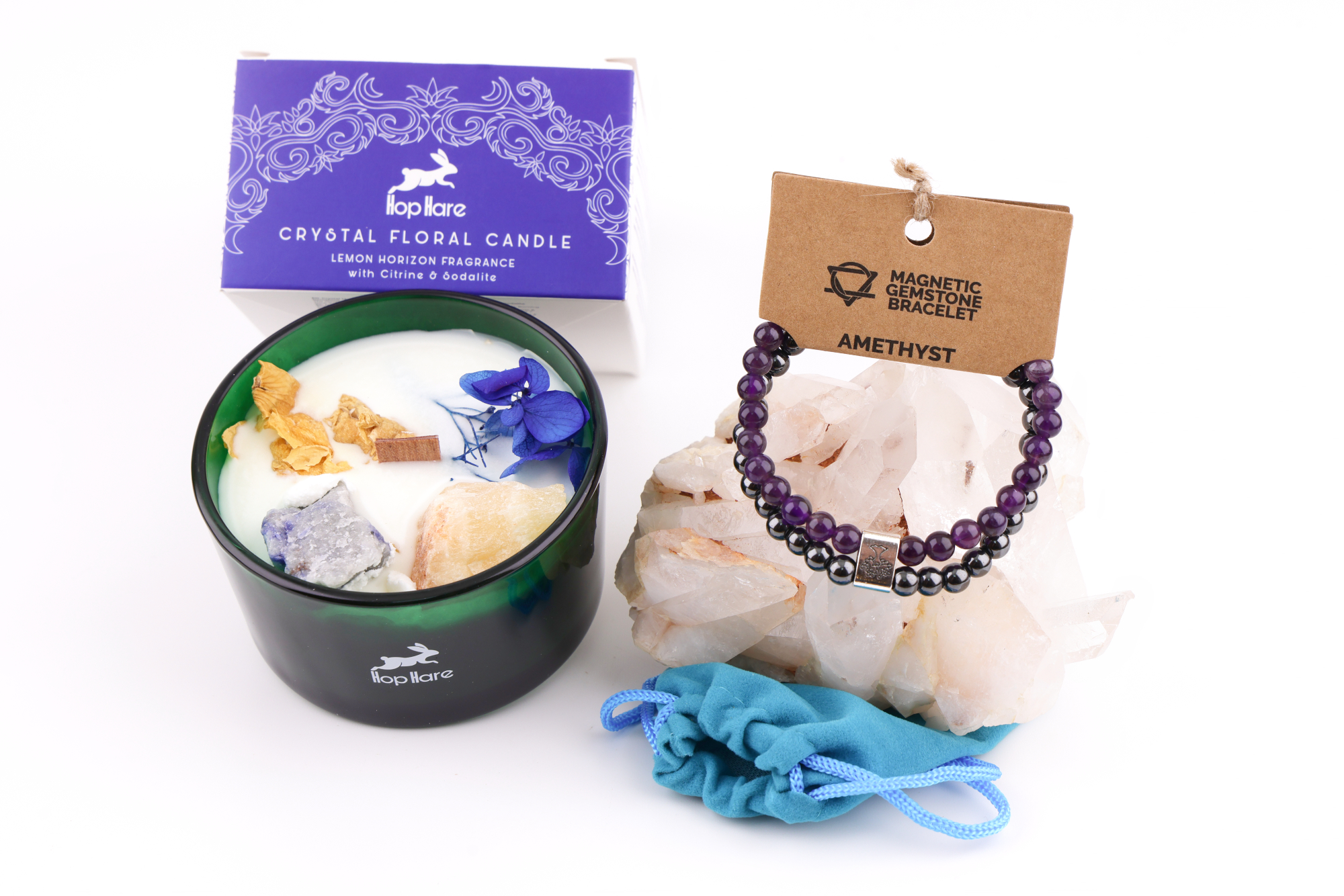 Grüne Hop‑Hare Duftkerze mit Citrin‑ und Amethyst‑Steinen sowie Blüten, daneben die lilafarbene Produktbox; rechts ein Amethyst‑Magnetarmband auf brauner Karte, präsentiert auf Bergkristallen mit türkisfarbenem Beutel.