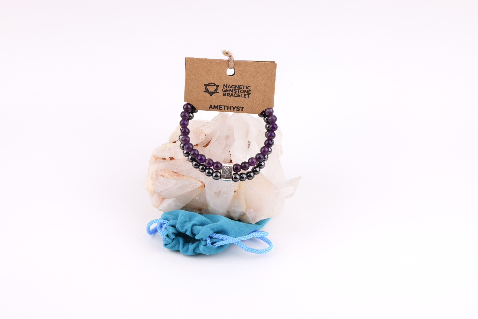 Amethyst‑Magnetarmband mit brauner Karte, präsentiert auf einem weißen Bergkristall‑Cluster mit türkisfarbenem Stoffbeutel im Hintergrund.