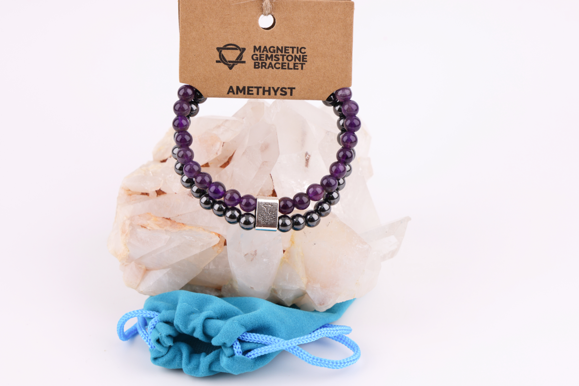 Amethyst‑Magnetarmband mit brauner Karte, präsentiert auf einem weißen Bergkristall‑Cluster mit türkisfarbenem Stoffbeutel im Hintergrund.