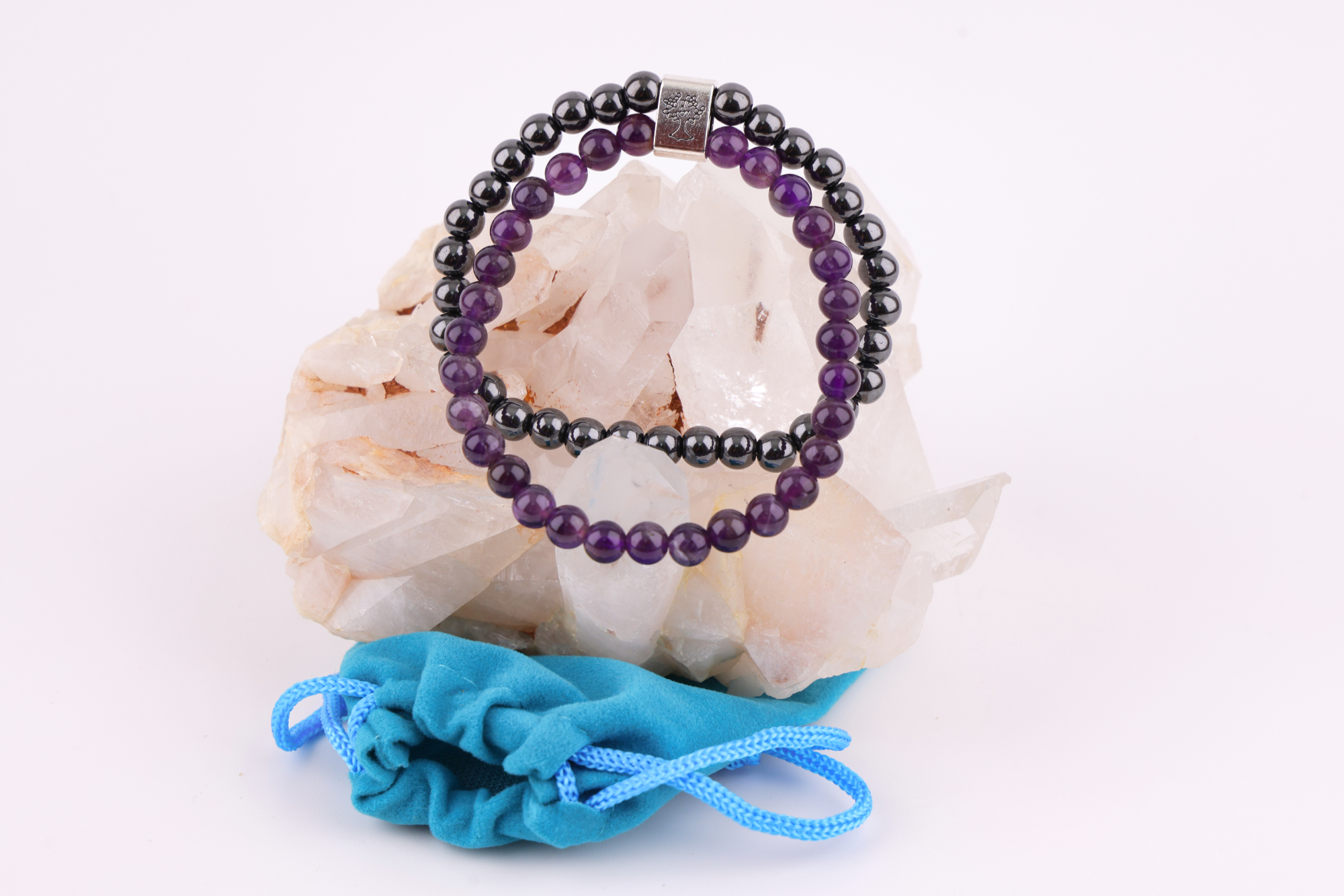 Amethyst‑Magnetarmband mit brauner Karte, präsentiert auf einem weißen Bergkristall‑Cluster mit türkisfarbenem Stoffbeutel im Hintergrund.