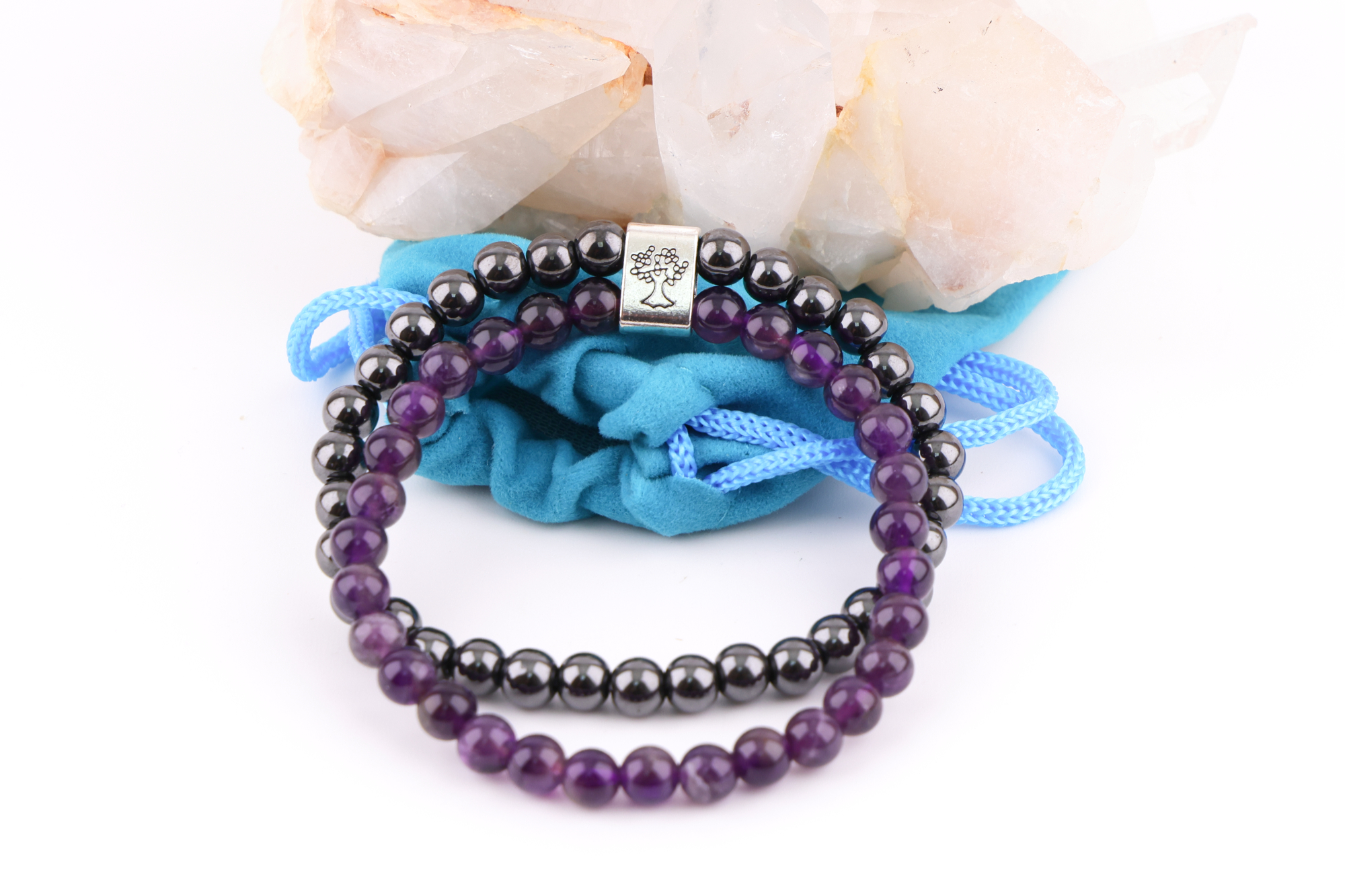 Amethyst‑Magnetarmband mit brauner Karte, präsentiert auf einem weißen Bergkristall‑Cluster mit türkisfarbenem Stoffbeutel im Hintergrund.