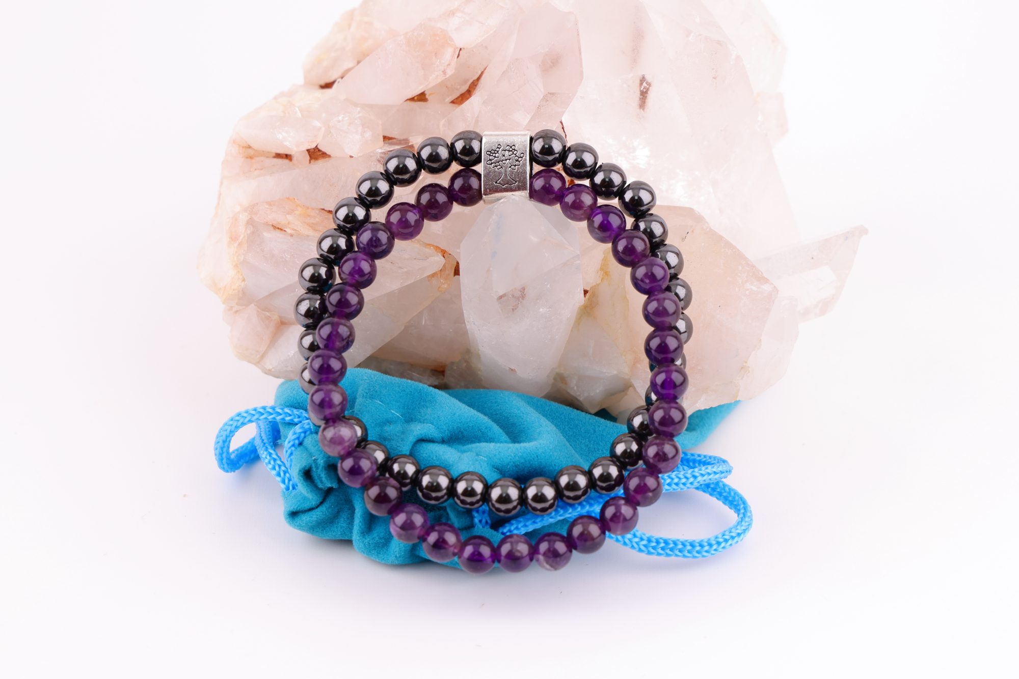 Amethyst‑Magnetarmband mit brauner Karte, präsentiert auf einem weißen Bergkristall‑Cluster mit türkisfarbenem Stoffbeutel im Hintergrund.