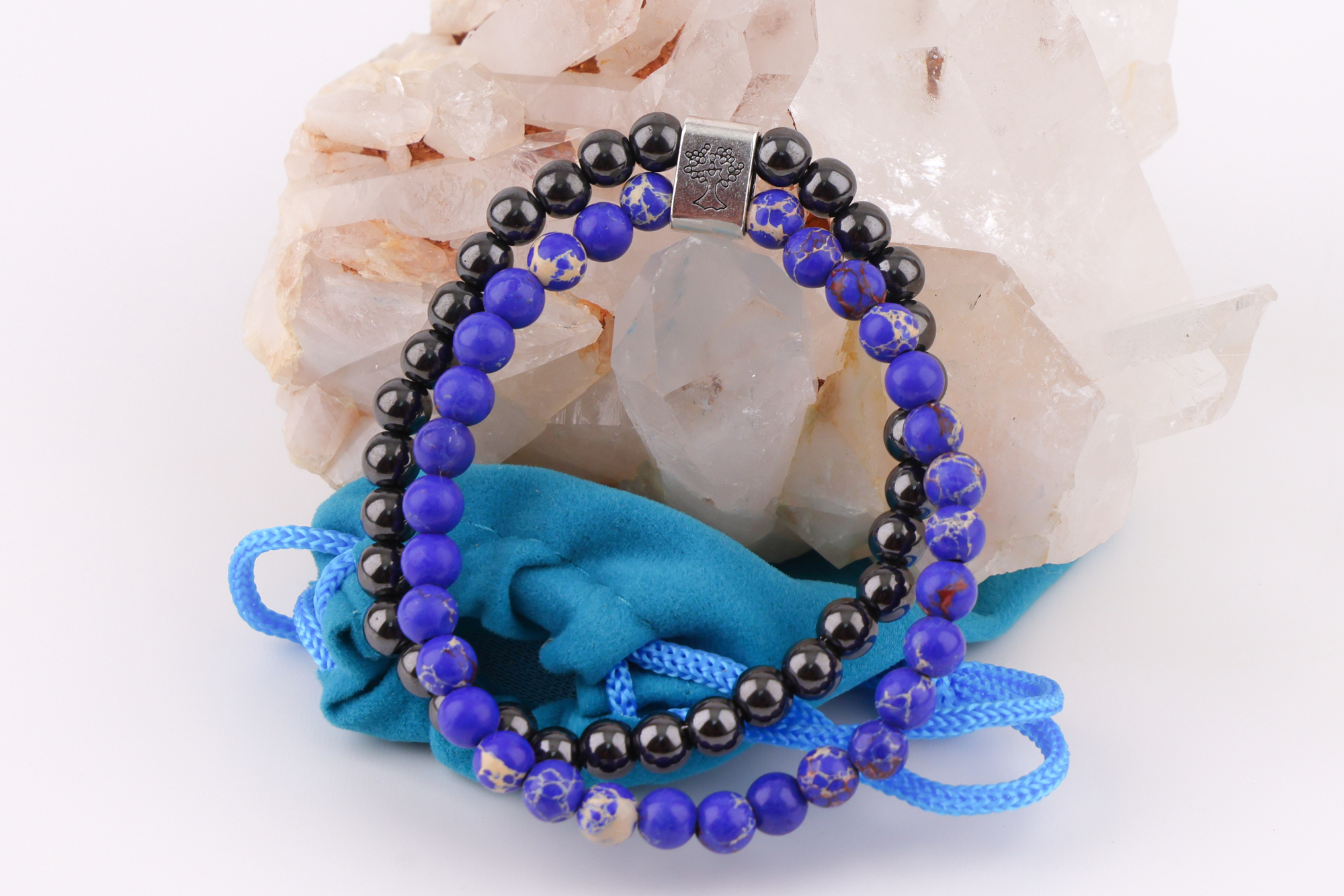 Sodalith‑Magnetarmband mit Baum‑Symbolverschluss auf Bergkristallen, daneben ein türkisfarbener Beutel.