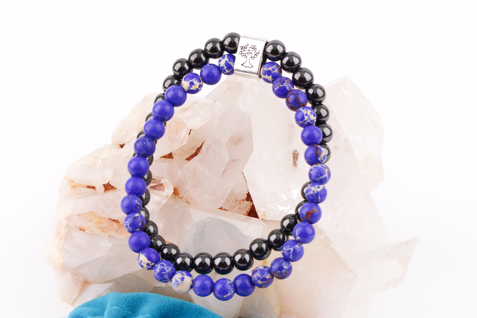 Sodalith‑Magnetarmband mit Baum‑Symbolverschluss auf Bergkristallen, daneben ein türkisfarbener Beutel.