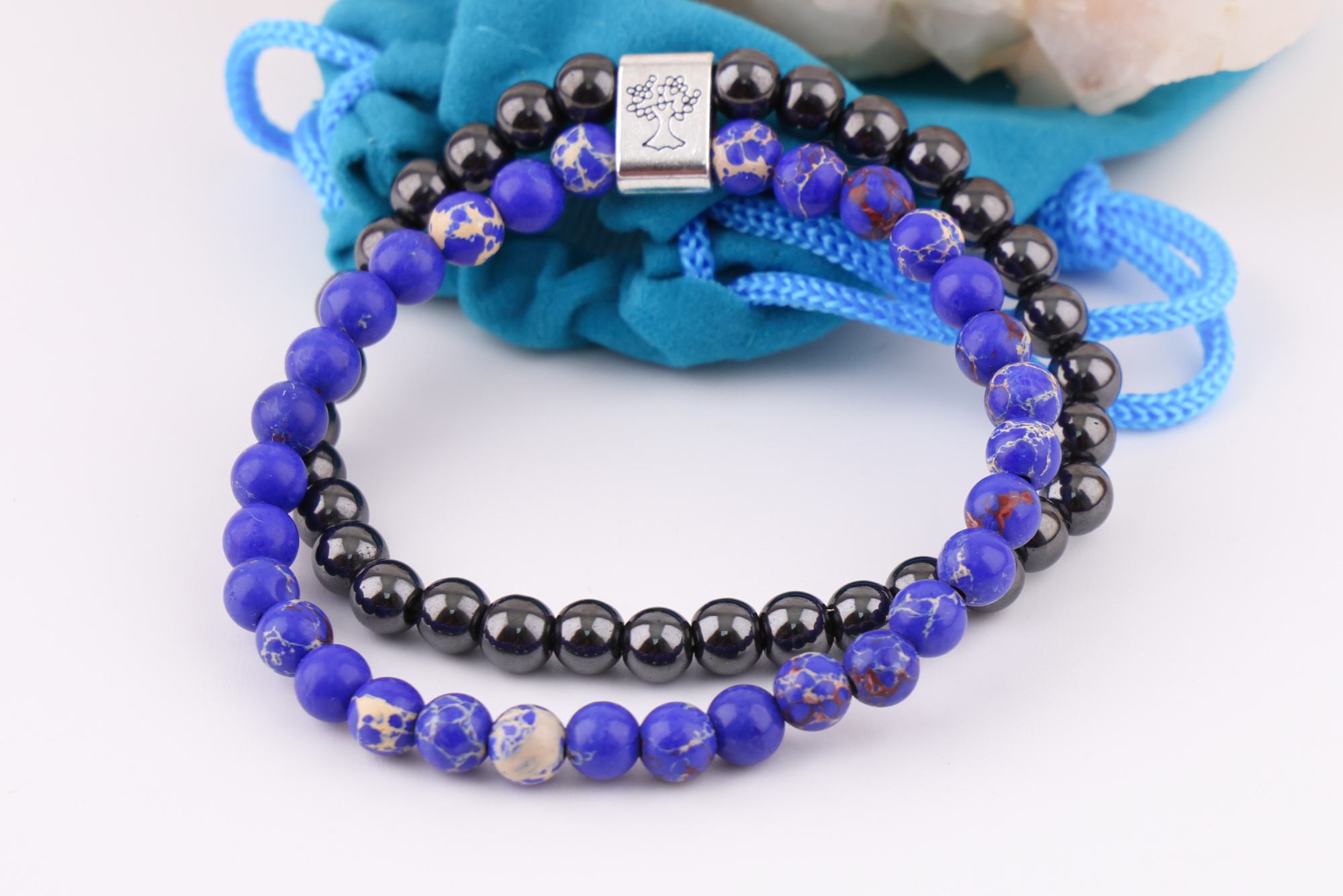 Sodalith‑Magnetarmband mit Baum‑Symbolverschluss auf Bergkristallen, daneben ein türkisfarbener Beutel.