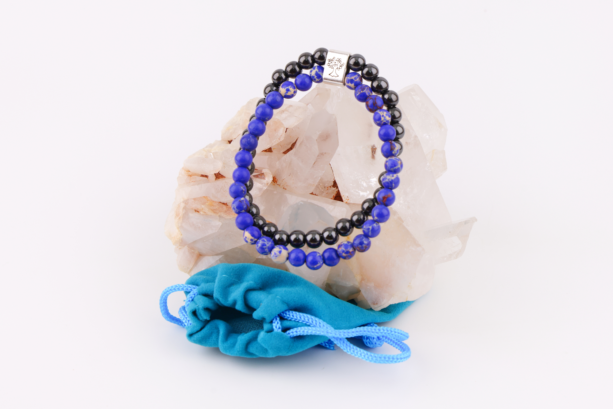 Sodalith‑Magnetarmband mit Baum‑Symbolverschluss auf Bergkristallen, daneben ein türkisfarbener Beutel.