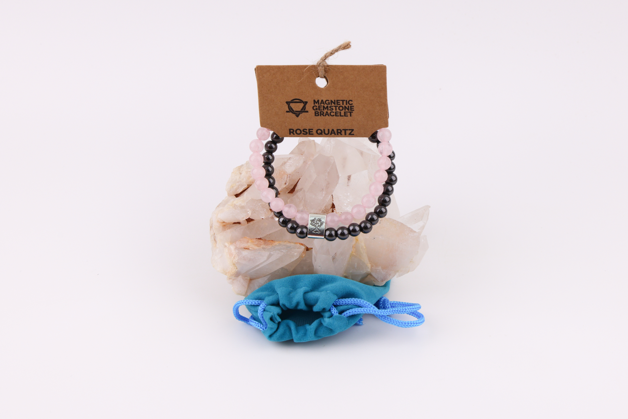 Rosenquarz‑Magnetarmband auf Rosenquarz‑Kristall mit blauem Schmuckbeutel.