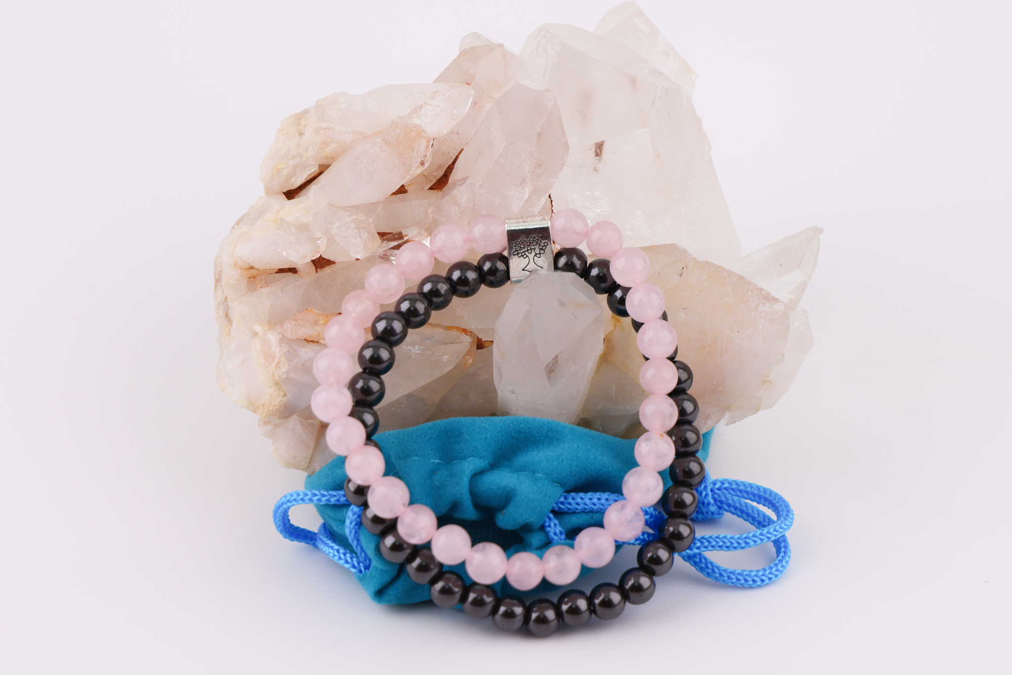 Rosenquarz‑Magnetarmband auf Rosenquarz‑Kristall mit blauem Schmuckbeutel.