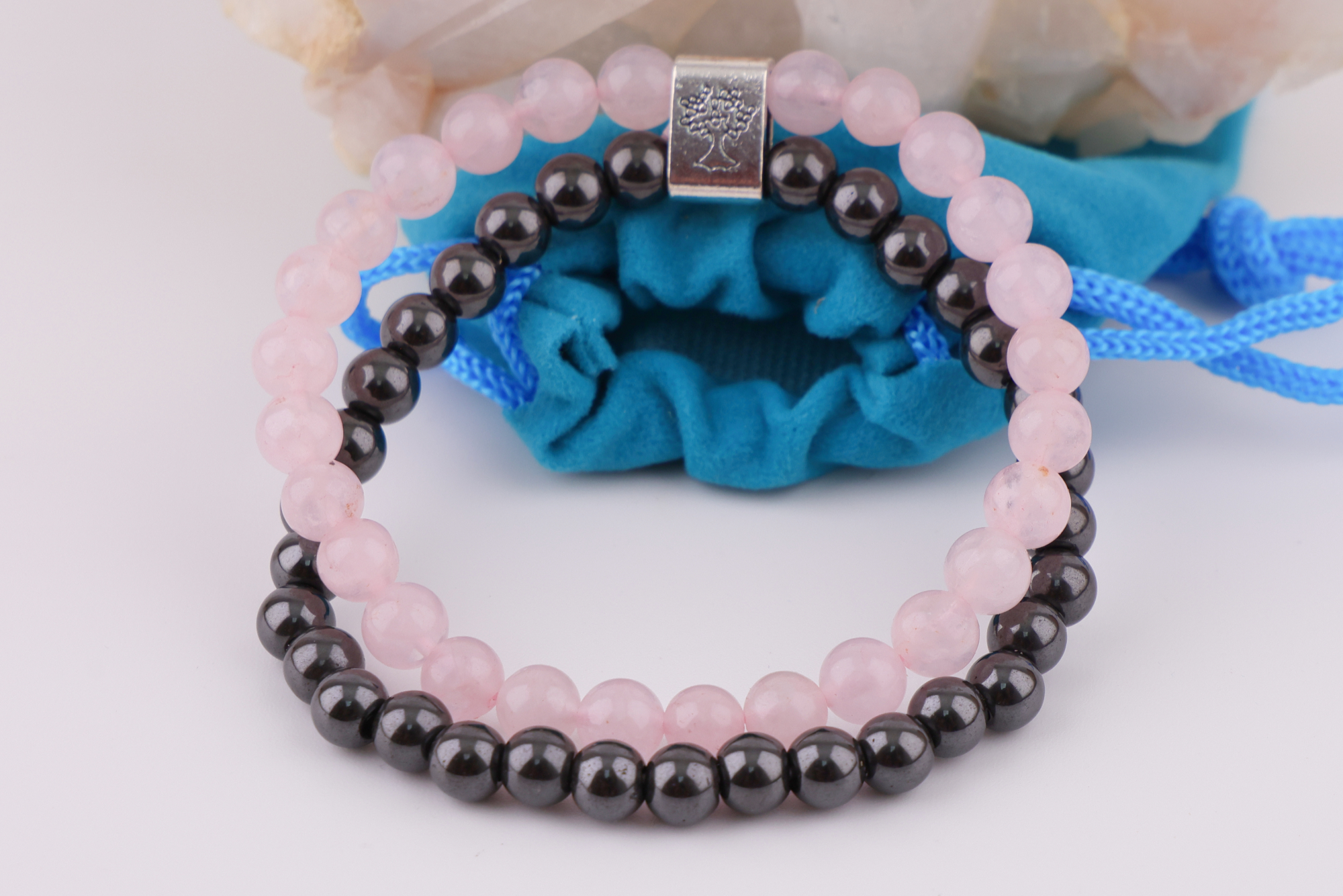 Rosenquarz‑Magnetarmband auf Rosenquarz‑Kristall mit blauem Schmuckbeutel.