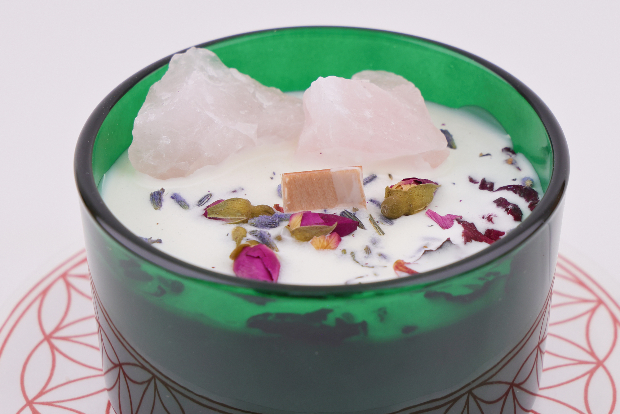 Grüne Glas‑Kerze mit dekorativem Rosenquarz und Blüten auf Musterplatte.