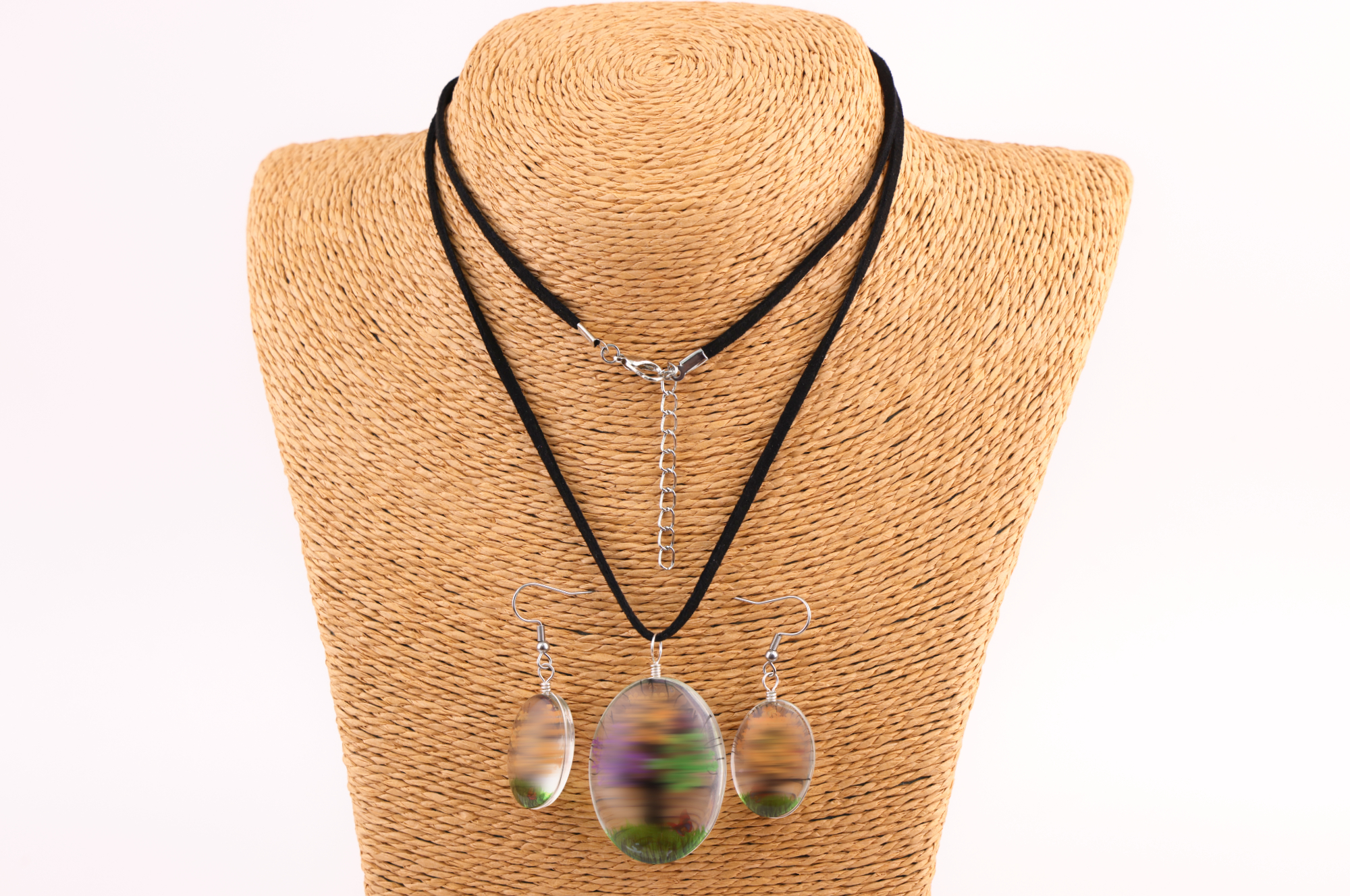 Schmuckset mit ovalem braun‑goldenem und buntem Anhänger sowie passenden Ohrringen, präsentiert auf einem gewebten Schmuckständer.