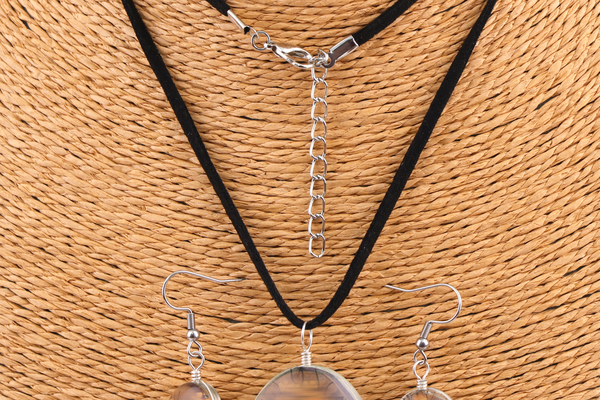 Schmuckset mit ovalem braun‑goldenem und buntem Anhänger sowie passenden Ohrringen, präsentiert auf einem gewebten Schmuckständer.