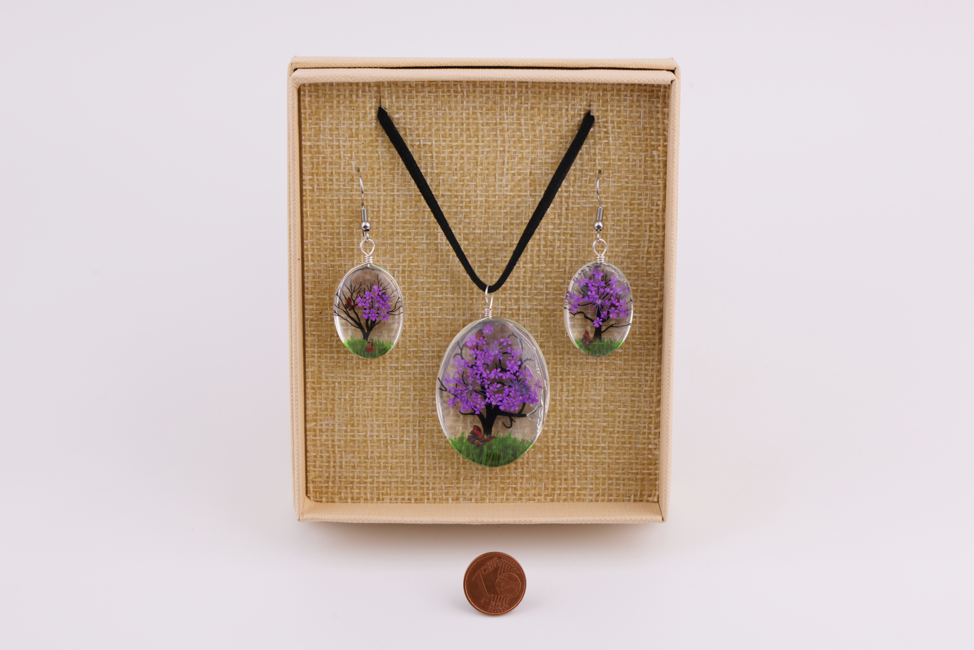 Baum‑des‑Lebens Schmuckset  Baum‑Motiv, bestehend aus Halsanhänger und Ohrringen in beige Geschenkbox, daneben eine Münze als Größenvergleich.