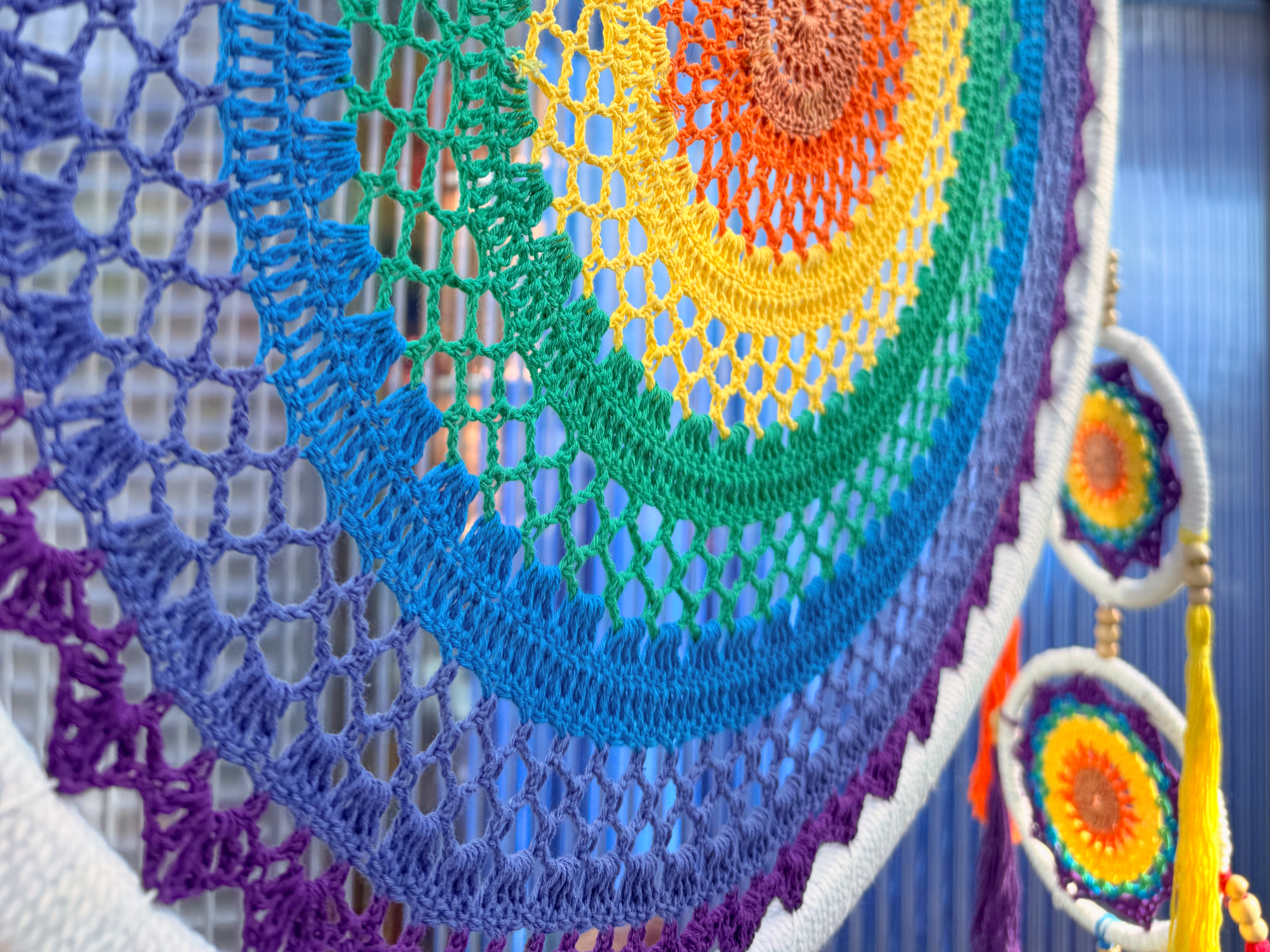 Nahaufnahme eines farbenfrohen, gehäkelten Traumfängers mit konzentrischen Regenbogenringen und kleineren, passenden Hängeelementen im Hintergrund.