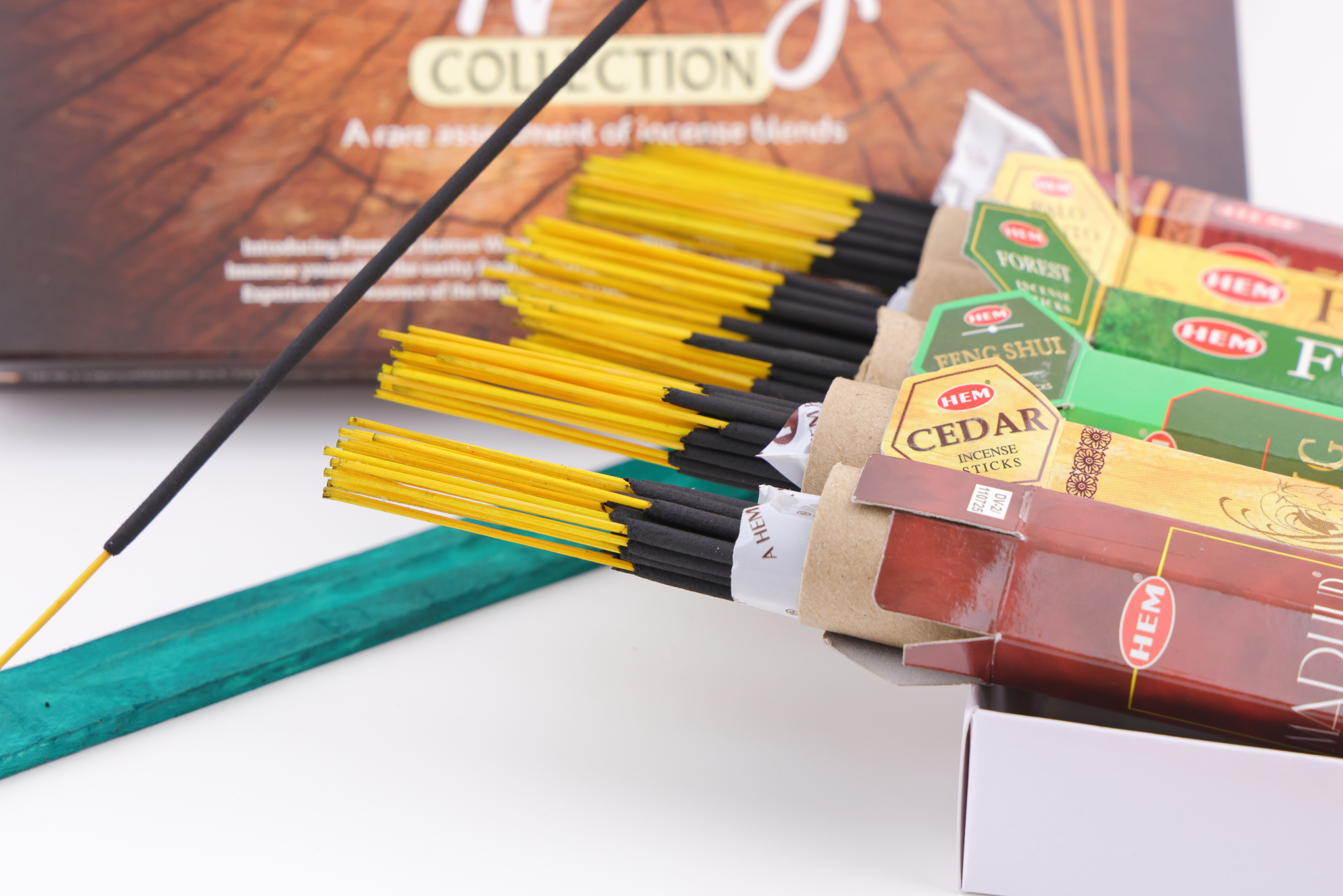 HEM Räucherwerk‑Set der Woody Collection mit verschiedenen Duftstäbchen‑Packungen (Cedar, Palo Santo, Foret, Feng Shui, Sandal), gelben Räucherstäbchen und grünem Halter.