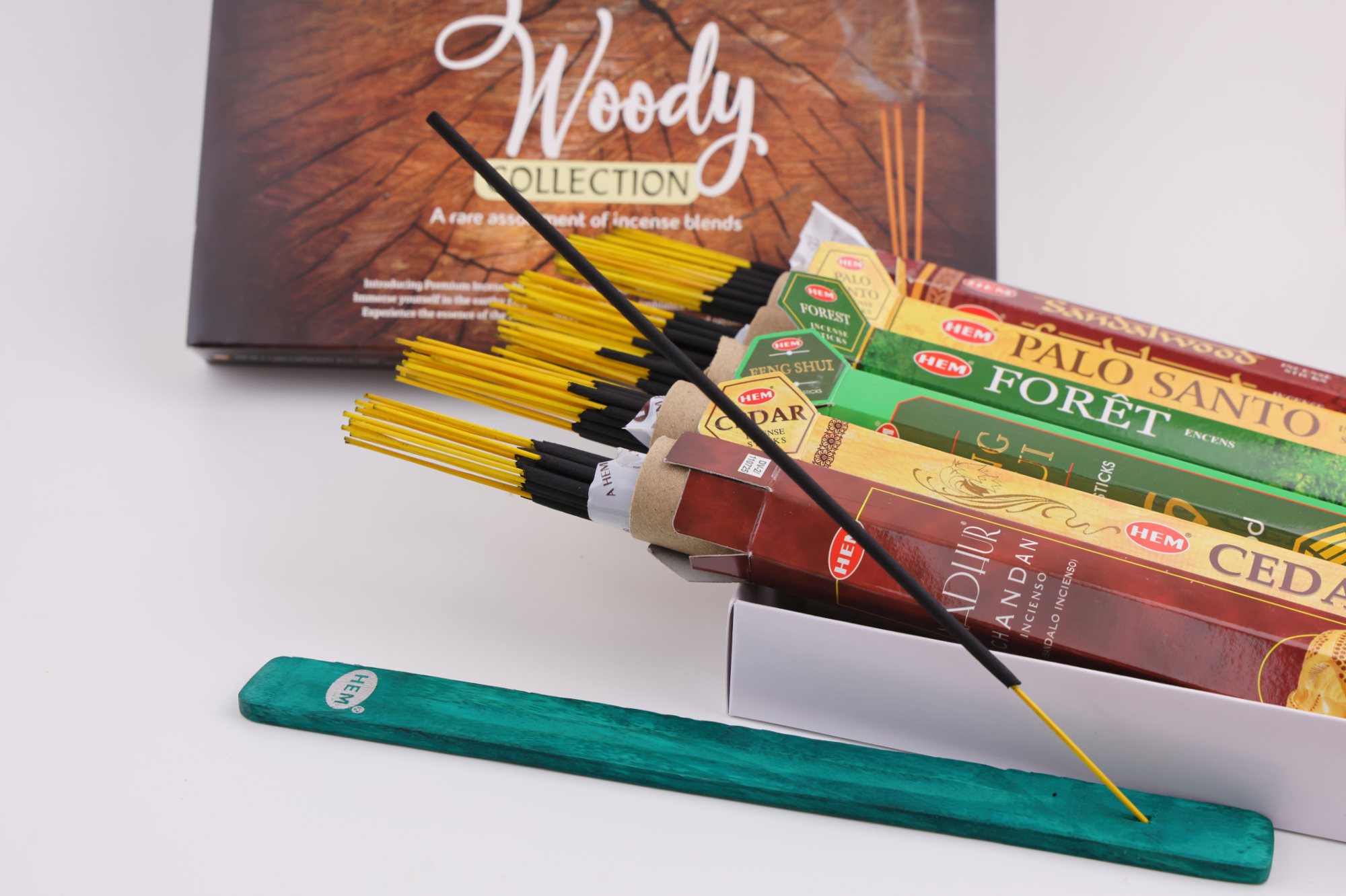 HEM Räucherwerk‑Set der Woody Collection mit verschiedenen Duftstäbchen‑Packungen (Cedar, Palo Santo, Foret, Feng Shui, Sandal), gelben Räucherstäbchen und grünem Halter.
