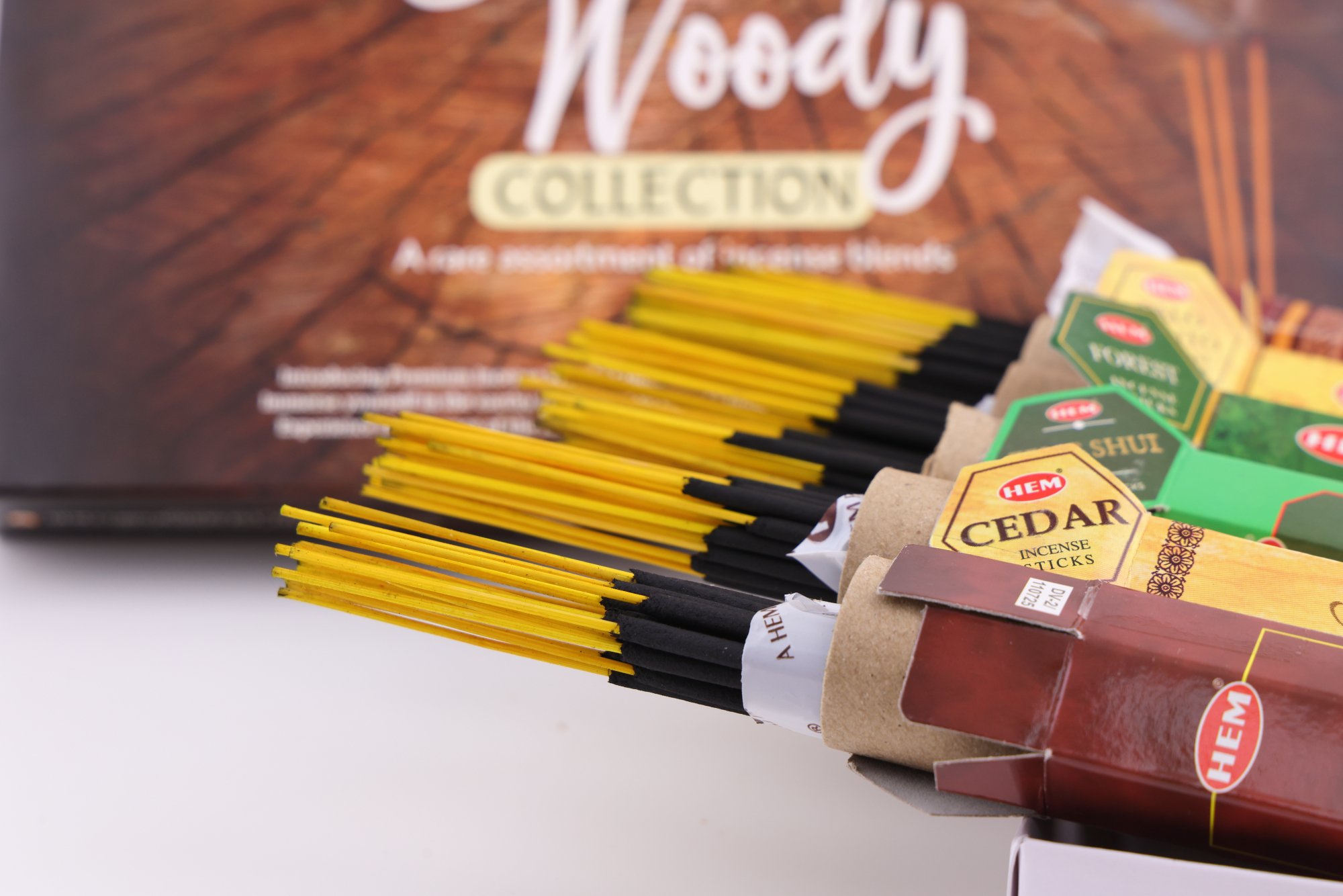 HEM Räucherwerk‑Set der Woody Collection mit verschiedenen Duftstäbchen‑Packungen (Cedar, Palo Santo, Foret, Feng Shui, Sandal), gelben Räucherstäbchen und grünem Halter.